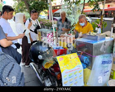 Mobiler Eisverkäufer auf der Straße in der Orchard Road, einem beliebten Dessert-Ort für Touristen, indonesische Dame, die Fotos von den 2 Männern macht. Singapur. Stockfoto