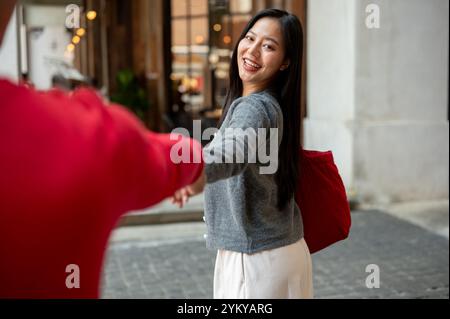 Ein charmantes, glückliches Mädchen aus Asien macht einen Stadtbummel und shoppen mit ihrem Freund, hält Hände und teilt süße Momente zusammen, während sie durchstreifen Stockfoto