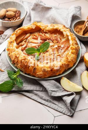 Frisch gebackene Apfelgalette, dekoriert mit Mandelflocken, Minzblättern, Zimt und Pekannüssen, serviert auf Keramikplatte Stockfoto