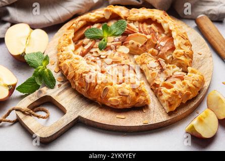 Frisch gebackene Apfelgalette, dekoriert mit Mandelflocken und Minzblättern, serviert auf einem Holzbrett Stockfoto