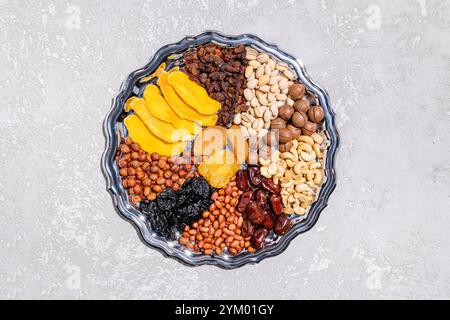 Eine große silberne Schale mit getrockneten Früchten und Nüssen auf grauem Zementhintergrund. Draufsicht. Ein Kopierbereich. Das Konzept des Tu be Shvat. Gesunde Ernährung Stockfoto