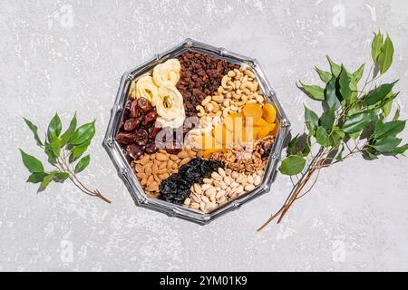 Ein großes silbernes Gericht mit traditionellen Leckereien für den jüdischen Feiertag von Tu Be Shvat und jungen grünen Ästen auf grauem Zementhintergrund. Draufsicht Stockfoto