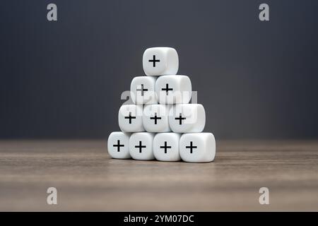Eine pyramidenförmige Anordnung von Würfeln mit Pluszeichen. Konzept für Wachstum, Fortschritt, Positivität und Mehrwert. Stockfoto
