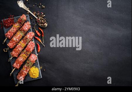 Roher Kebab mit Gewürzen auf einem schwarzen Tisch Stockfoto