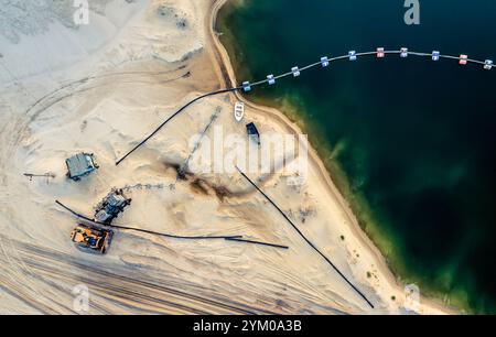 Luftaufnahme von Maschinen und Bergwerksausrüstung in der Nähe eines tiefblauen Sees auf sandiger Oberfläche Stockfoto