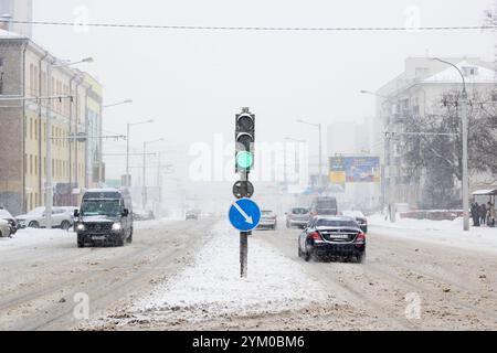 Weißrussland, Minsk - 20. november 2023: Alle Autos fahren ständig eine verschneite Straße hinunter, wo eine helle grüne Ampel das Inter beleuchtet Stockfoto