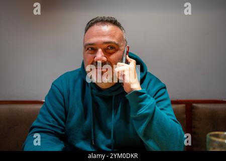 Bärtiger Mann, der in einem Restaurant sitzt, telefoniert und lächelt Stockfoto