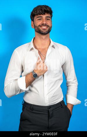 Porträt eines selbstbewussten Geschäftsmannes, der sein weißes Hemd vor einem leuchtend blauen Hintergrund anpasst Stockfoto