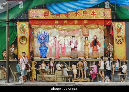 Ein Mann posiert vor einem Wandgemälde von Yip Yew Chong, das eine kantonesische Opernaufführung von Zeiten vergangener Zeiten darstellt; Temple Street, Chinatown, Singapur Stockfoto