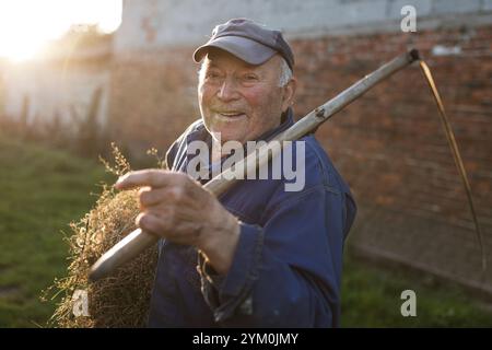 TYMOWA, POLEN - 29. MAI 2019: Alter Landwirt mit der Sense auf einem kleinen Bauernhof, der heutzutage unrentabel ist. Stockfoto