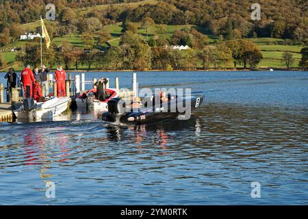 Eine Gruppe von Personen, die zwei andere in einem schwarzen Motorboot beobachten, das einen Steg oder Dock auf Coniston Water bei der Coniston Power Boat Records Week 2021 verlässt Stockfoto