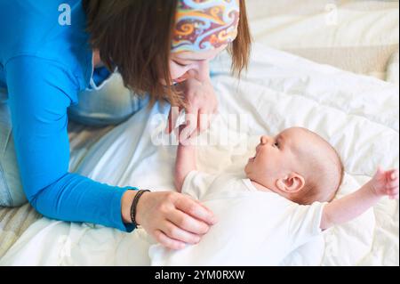 Mutter genießt einen verspielten Moment mit ihrem Baby auf einem gemütlichen Bett am Nachmittag Stockfoto