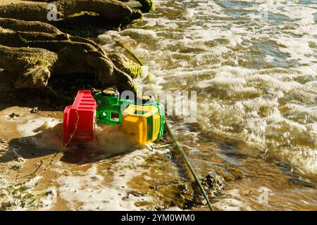 Ein lebendiger Spielzeugwagen liegt am Sandstrand, der teilweise unter Wasser liegt, während die Wellen über ihn strömen. Diese verspielte Szene fängt einen Moment der Kindheit des ein Stockfoto