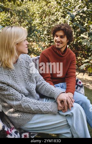 Zwei junge Menschen unterhalten sich in einem üppigen Garten, gekleidet in stilvolle Pullover, umgeben von Grün, reflektieren Wärme und Verbundenheit o Stockfoto