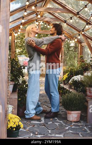 Inmitten lebendiger Blumen und warmer Lichter teilt sich ein junges Paar eine liebevolle Umarmung in einem gemütlichen Gewächshaus. Ihr Lachen erfüllt die Luft und feiert lov Stockfoto