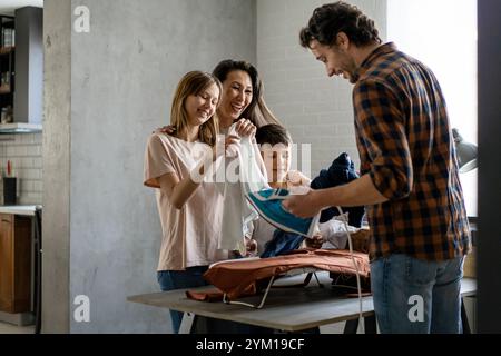 Glückliche Familie gemischter Rasse, die gemeinsam Hausarbeiten macht, bügelt, Haushalt zu Hause zusammen. Stockfoto