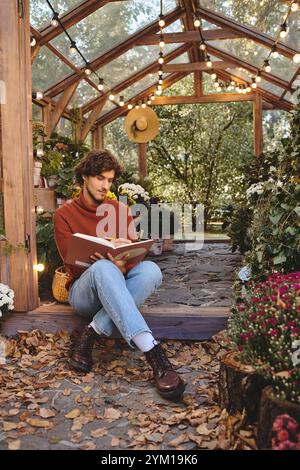 Ein junger Mann sitzt bequem auf einem Steinweg und genießt die friedliche Atmosphäre eines lebendigen Gewächshauses voller farbenfroher flo Stockfoto