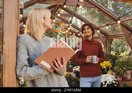 In einem ruhigen Gewächshaus voller lebendiger Pflanzen unterhalten sich junge schwule Paare mit Liebe und Liebe. Einer hält ein Buch, der andere genießt Dampf Stockfoto