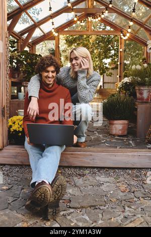 Zwei junge Männer teilen einen freudigen Moment in einem schönen Gewächshaus voller Pflanzen und Blumen. Stockfoto