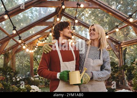 In einem bezaubernden Gewächshaus voller Grün steht ein junges Paar nahe und teilt ein Lächeln. Stockfoto