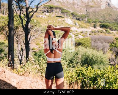 Rückansicht einer jungen schlanken Frau, die ihre Hände vor dem Training in der Natur spannt. Rückansicht einer Sportlerin, die ihre Hände aufwärmt. Stockfoto