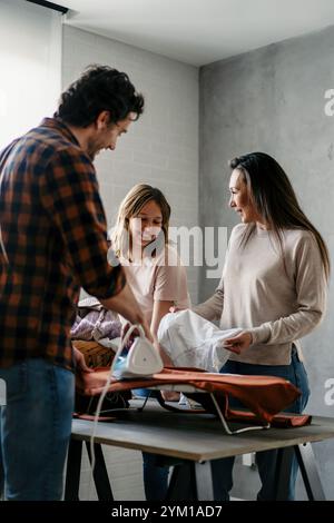 Glückliche Familie gemischter Rasse, die gemeinsam Hausarbeiten macht, bügelt, Haushalt zu Hause zusammen. Stockfoto