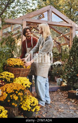 In einem bezaubernden Gewächshaus voller leuchtender gelber Blumen teilt das junge schwule Paar einen Moment der Freude, während es wunderschöne Blüten arrangiert. Warm Stockfoto