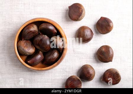 Süße Kastanien in einer Holzschale auf Leinen. Roh, ganz und ungeschälte Castanea sativa, kann roh, kandiert, gekocht, zu Mehl gemahlen usw. gegessen werden Stockfoto