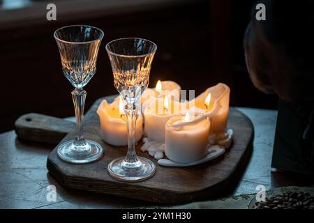 Wachskerzen brennen auf einem Holzbrett oder Tisch und ein paar Vintage Kristallgläser, gemütlich, warm und dunkel Hintergrund, Nahaufnahme Stockfoto