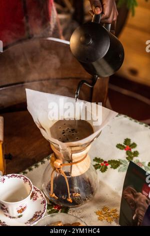 Gießen Sie Filterkaffee über eine alternative Brühmethode. Mädchen gießt heißes Wasser über geröstete und gemahlene Kaffeebohnen, die im Papierfilter enthalten sind. Keramik Stockfoto