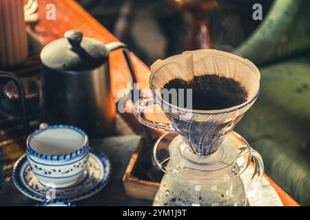 Gießen Sie Filterkaffee über eine alternative Brühmethode. Mädchen gießt heißes Wasser über geröstete und gemahlene Kaffeebohnen, die im Papierfilter enthalten sind. Keramik Stockfoto