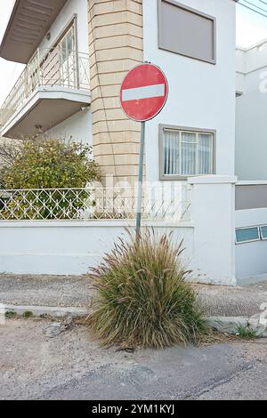 Verkehrsschild No Entry, umgeben von Gras vor einem Wohngebäude an einer Stadtstraße Stockfoto