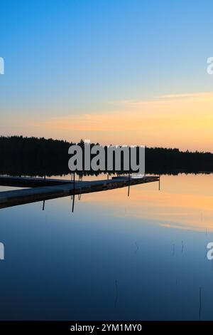 Holzsteg bei Sonnenuntergang auf einem schwedischen See. Die Farben des Sonnenuntergangs spiegeln sich im Wasser wider. Ein Badesee in der skandinavischen Landschaft Stockfoto