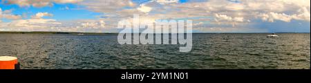 Stürmischer Himmel über einem See. Dunkle Wolken stehen im Kontrast zu Sonnenstrahlen, die das Wasser glitzern lassen Stockfoto