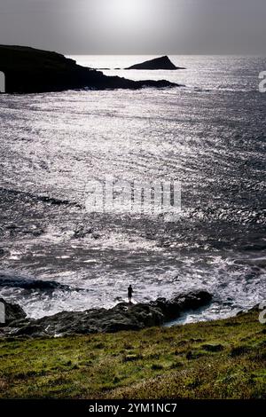 Abendlicht über der Silhouette eines Anglers, der von den Felsen von Crantock aus fischt, mit der felsigen Insel The Chick im Hintergrund an der Küste von Newqua Stockfoto