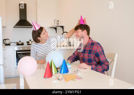 Das junge Paar feiert zu Hause gemütlich Geburtstag und genießt Kuchen und Lachen in warmer Atmosphäre. Fröhliche Atmosphäre, farbenfrohe Dekoration, Vorbereitung auf die Feiertagsparty, Dekoration Küchenraum Stockfoto