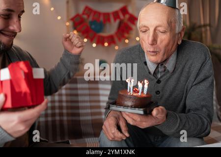 Der liebevolle Millennial Sohn wünscht Vater alles Gute zum Geburtstag des alten Mannes bläst Kerzen auf Kuchen nach Hause Geburtstag Stockfoto