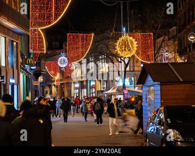 Straßburg, Frankreich - 23. Dezember 2023: Festliche Straßenszene am Abend in Straßburg mit Weihnachtsbeleuchtung, Dekoration und Menschen, die in einer Urlaubsatmosphäre durch das beleuchtete Stadtzentrum schlendern Stockfoto