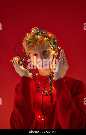 Ein Mann zeigt seine einzigartige Weihnachtsmode, indem er sich spielerisch in farbenfrohe Weihnachtslichter verschlingt. Stockfoto