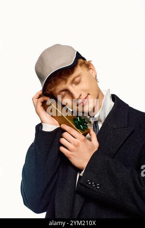 Ein stilvoller Mann in festlicher Kleidung genießt einen fröhlichen Moment, während er ein wunderschön verpacktes Weihnachtsgeschenk hält. Das Ambiente strahlt Feiertagsstimmung aus wie er Stockfoto