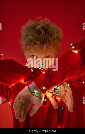 Ein junger Mann zeigt festliche Weihnachtsmode mit hellen Weihnachtslichtern um seine Arme. Stockfoto