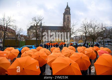 Magdeburg, Deutschland. November 2024. Dutzende Männer und Frauen mit orangen Regenschirmen stehen vor dem landtag Sachsen-Anhalt. Die Kathedrale ist im Hintergrund zu sehen. Mit der Aktion des Landesfrauenrates Sachsen-Anhalt zum Internationalen Tag gegen Gewalt gegen Frauen soll auf die Notwendigkeit hingewiesen werden, das Gewaltpräventionsgesetz auf Bundesebene zu verabschieden. Die Regenschirme symbolisierten den Schutz vor Gewalt gegen Frauen. Quelle: Klaus-Dietmar Gabbert/dpa/Alamy Live News Stockfoto