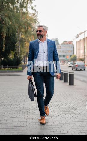 Ein gutaussehender reifer Geschäftsmann läuft durch die Straße der Stadt. Stockfoto