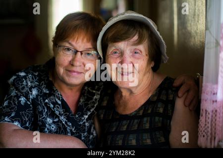 Eine ältere Frau posiert mit ihrer erwachsenen Tochter mittleren Alters für ein Porträt, beide lächeln herzlich und halten eine schöne Familienverbindung fest. Stockfoto