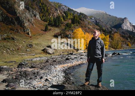 Ein männlicher Reisender steht am Ufer eines Gebirgsflusses in der Republik Altai und bestaunt das schnell fließende Wasser und die zerklüftete Landschaft. Stockfoto