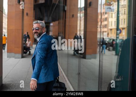 Ein gutaussehender reifer Geschäftsmann läuft durch die Straße in der Nähe des Bürogebäudes. Stockfoto