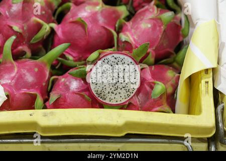 Die in zwei Hälften geschnittene Drachenfrucht zeigt das Fleisch darin, wird auf einen Korb gelegt. Drachenfrüchte stapeln sich in einem gelben Korb. Stockfoto