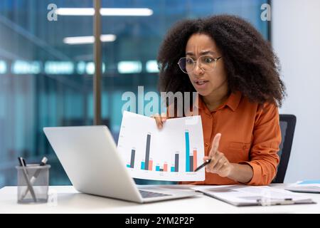 Afroamerikanische Geschäftsfrau im modernen Büro, die Balkendiagramme auf Laptop analysiert. Professionelle Präsentation von Dateneinblicken und Teilnahme an Besprechungen zur Geschäftsstrategie. Stockfoto