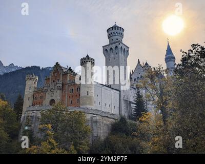 Eine majestätische mittelalterliche Burg mit hohen Türmen, umgeben von einem Wald im Herbst mit der Sonne am Himmel, Schloss Neuschwanstein beleuchtet vom Krieg Stockfoto