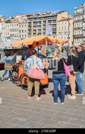 Marseille. Frankreich - 20. November 2024: Straßenhändler am Alten Hafen von Marseille, der Fisch auf einem Dreirad grillt. Das Bild fängt den lebhaften Markt ein Stockfoto